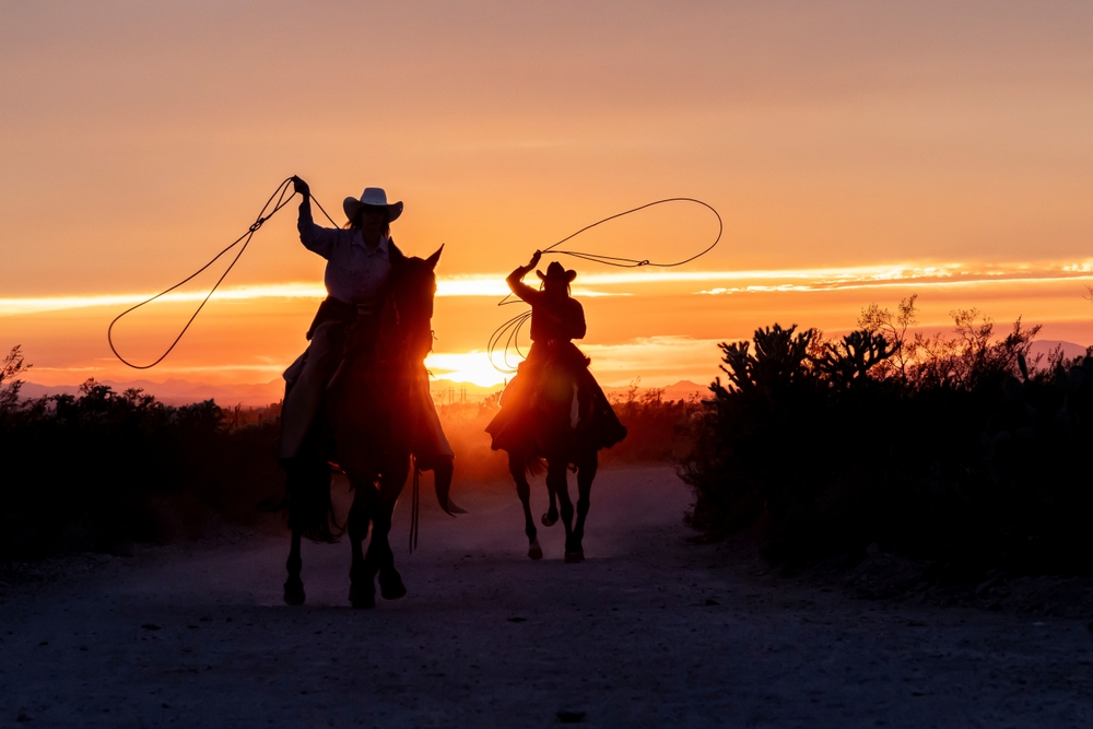 Female ranch hands, or cowgirls, riding horses in the sunset on a ranch in Arizona, USA