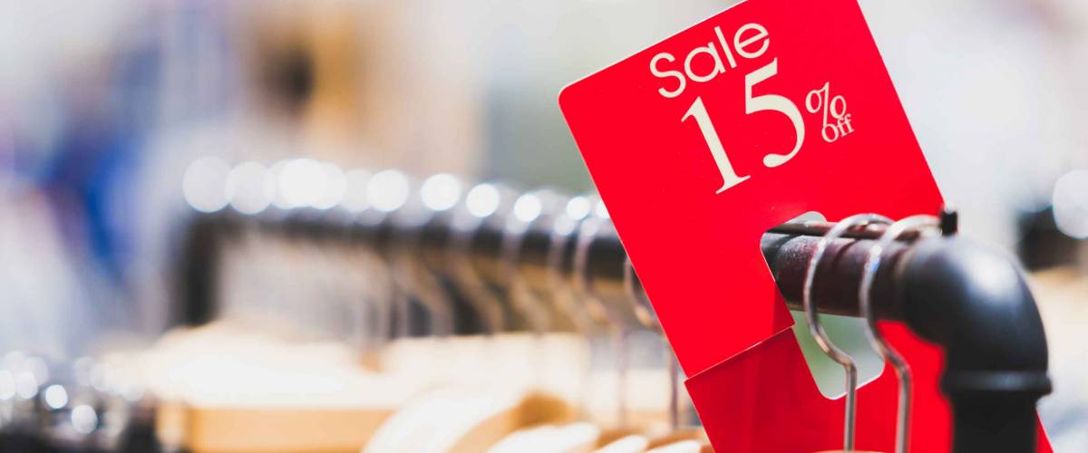 Red sale sign 15% discount on clothing rack in modern shopping mall