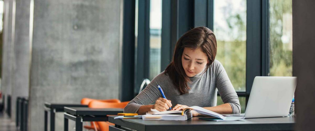 Shot of young asian female student sitting at table and writing on notebook. Young female student studying in library.